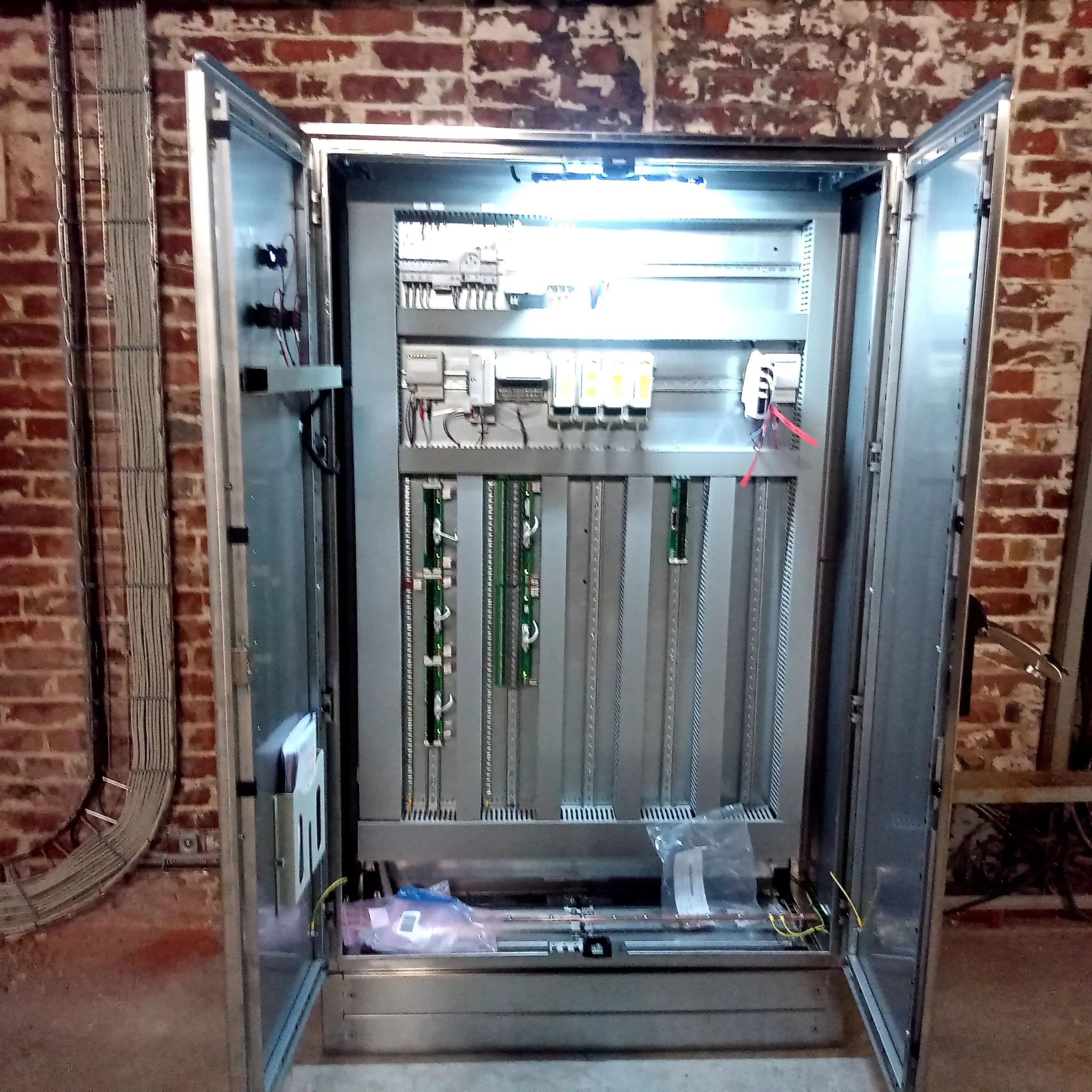 Armoire d'automatisme en acier inoxydable double porte en cours d'intégration et de câblage sur platine.
