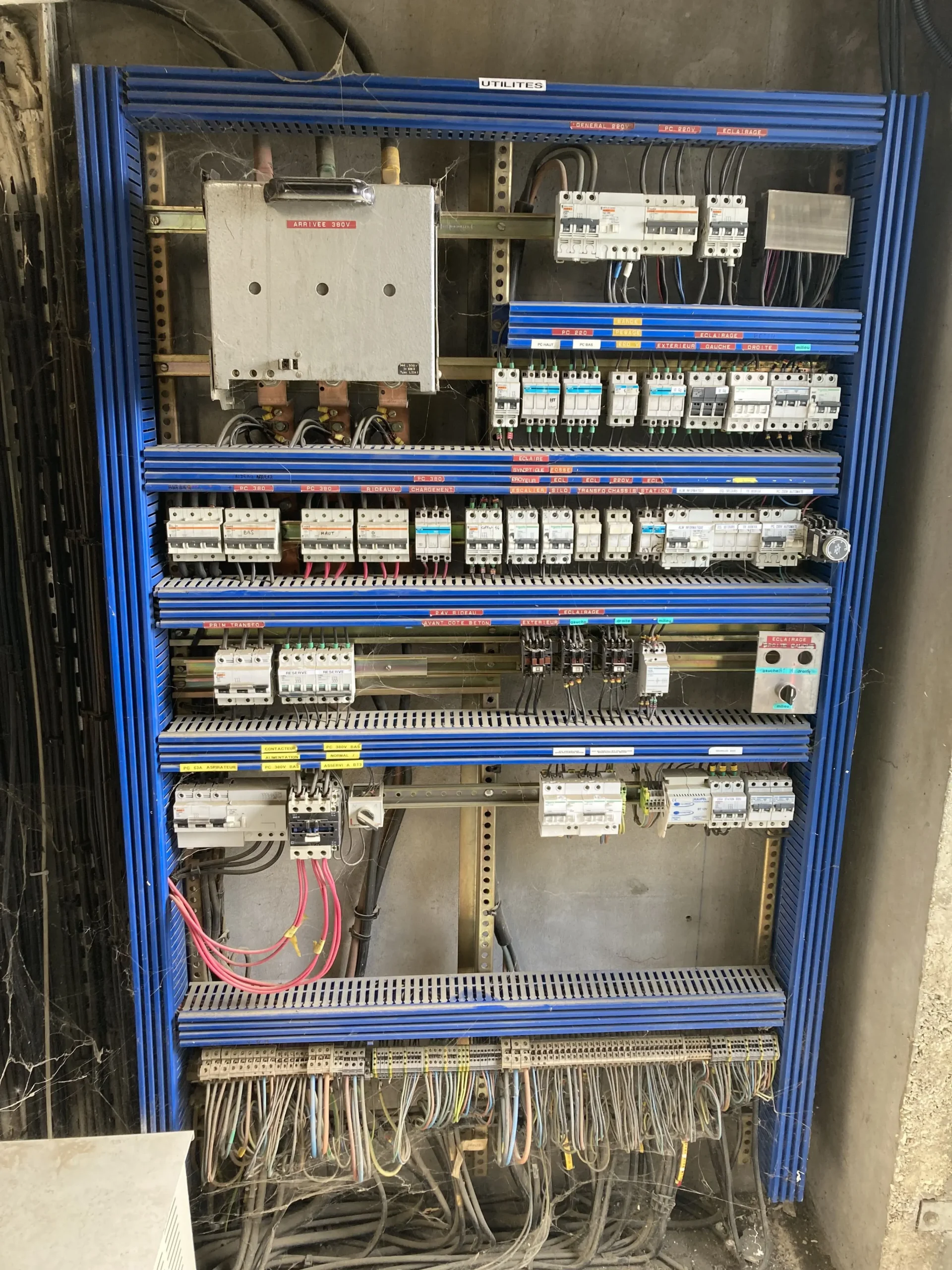 Grand tableau électrique industriel à structure bleue avec disjoncteurs, étiquettes de câblage et réseau de fils